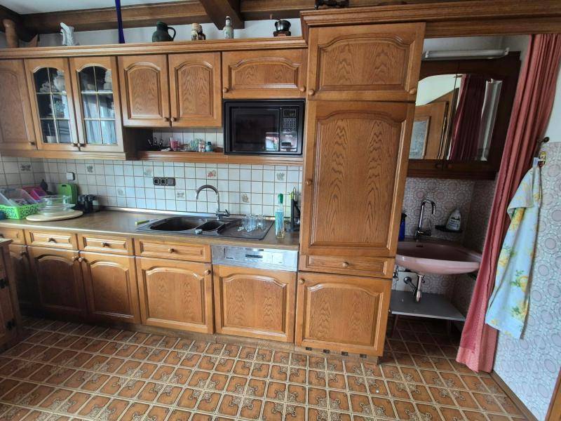 Rustikale Holzküche mit Fliesenboden und integrierten Geräten, daneben ein kleiner Waschbereich.