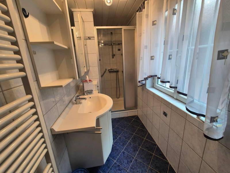 Funktionales Badezimmer mit Waschbecken, Duschkabine, Fenster und beheiztem Handtuchhalter.