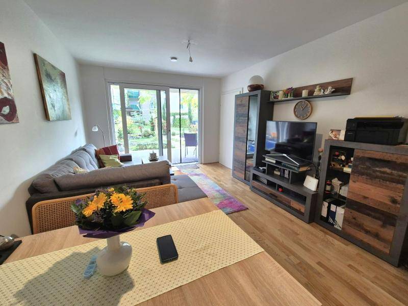 Heller Wohn- und Essbereich mit Holzboden, bequemer Couch und Zugang zum grünen Garten.