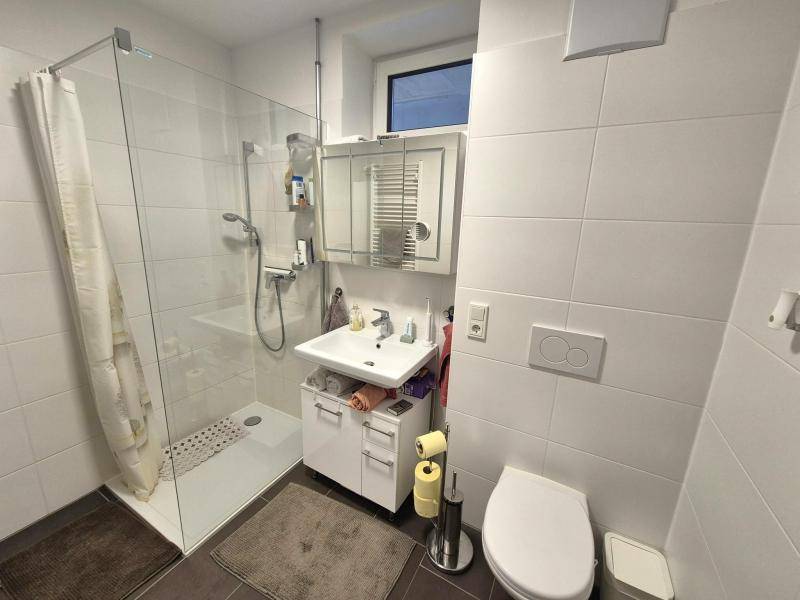 Modernes Badezimmer mit ebenerdiger Dusche, WC, Waschbecken und Fenster für Tageslicht.