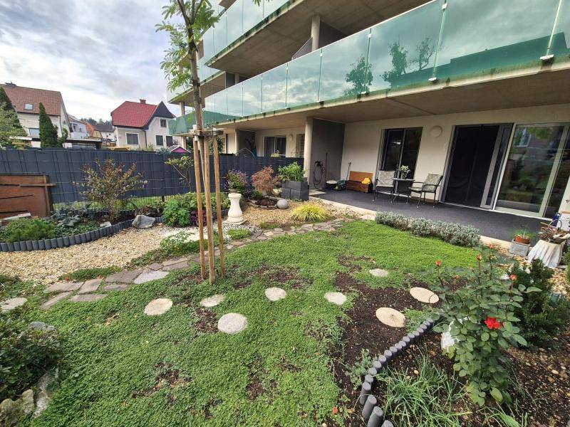 Gepflegter Gartenbereich mit blühenden Pflanzen und Blick auf die moderne Wohnanlage mit Balkonen.