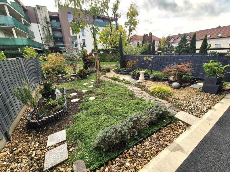 Vielfältiger Garten mit verschiedenen Pflanzen, Kieswegen, Trittsteinen und Zaunbegrenzung.