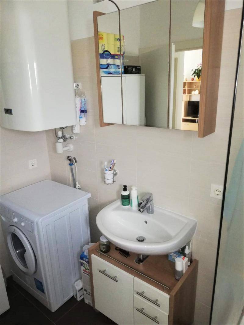 Badezimmer mit Waschmaschine, Waschbecken und Spiegelschrank.