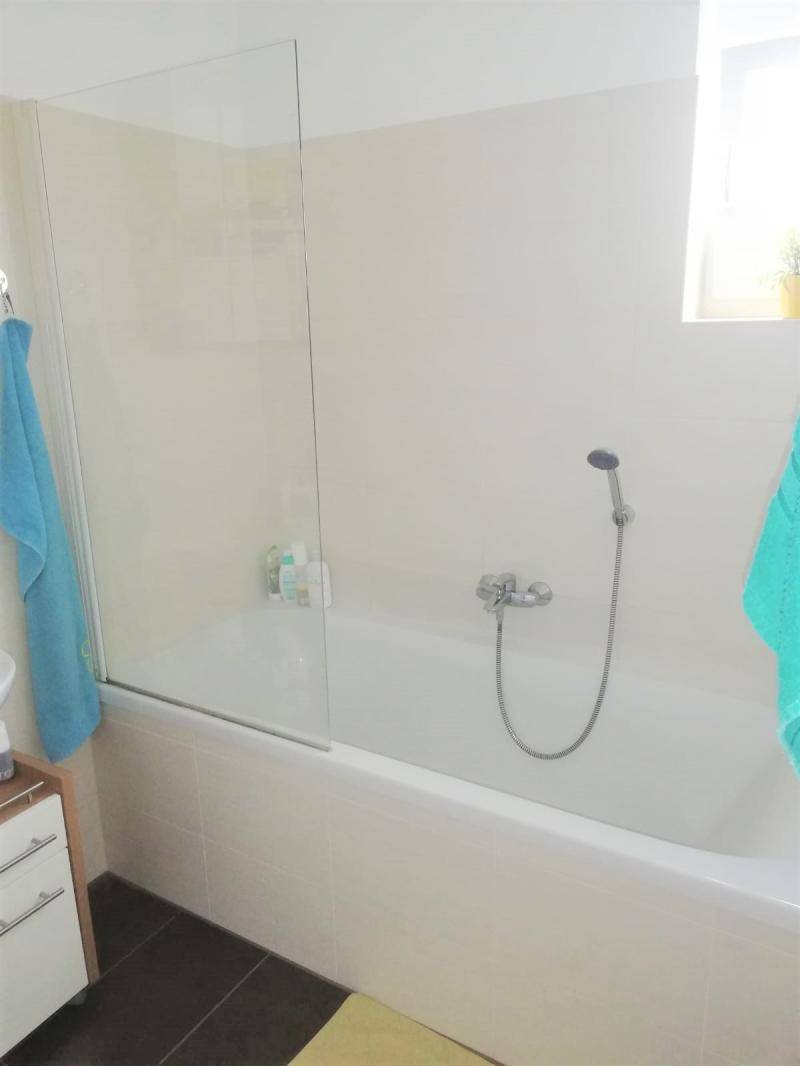 Badezimmer mit Badewanne, Duschabtrennung aus Glas und kleinem Fenster.
