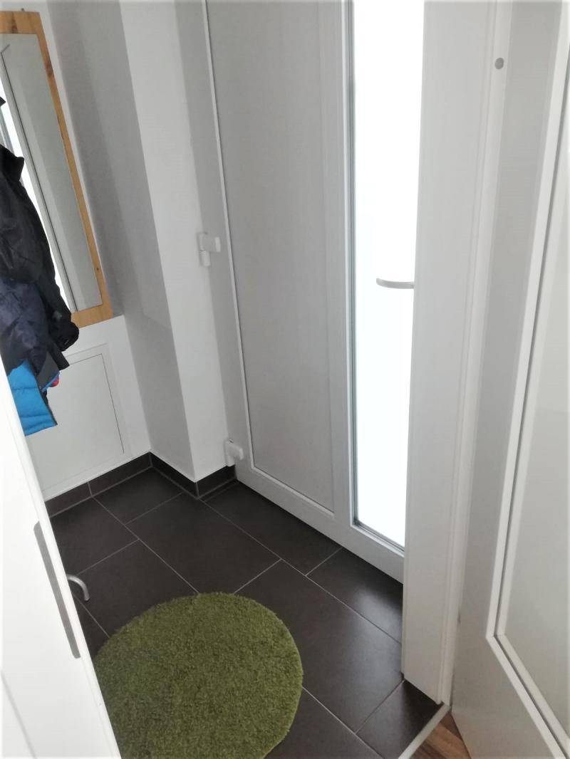 Eingangsbereich mit dunklen Fliesen, Garderobe und heller Tür zum Außenbereich.