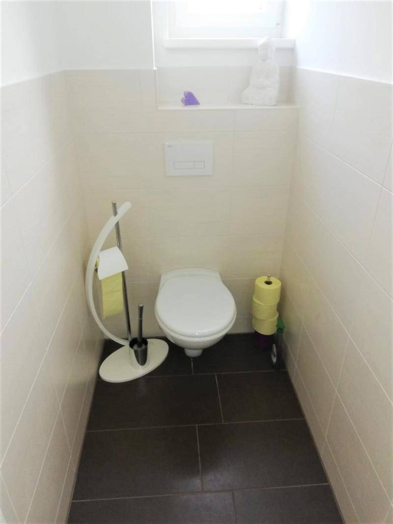 Separate Toilette mit wandhängendem WC, dunklen Fliesen und kleinem Fenster.