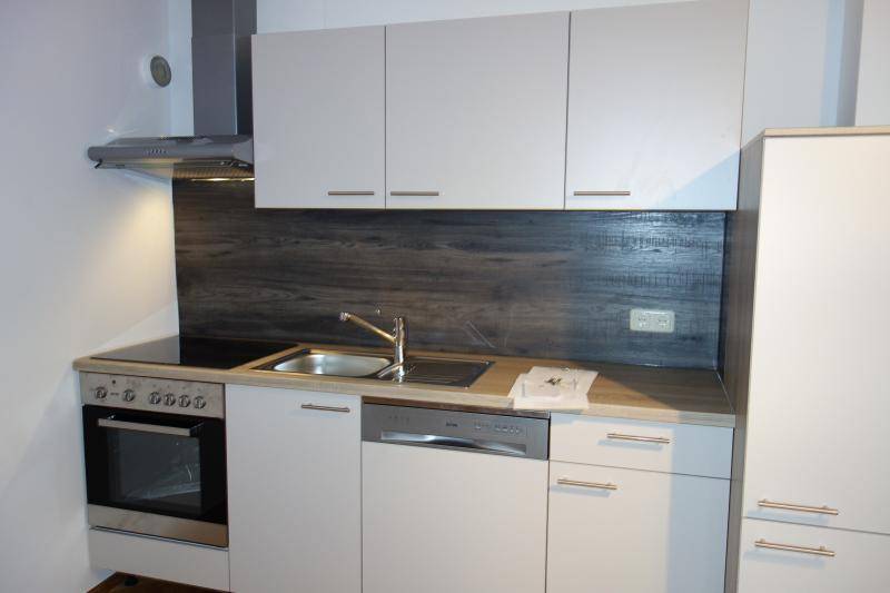 Moderne Einbauküche mit hellgrauen Schränken, Edelstahlgeräten und dunkler Holzoptik-Rückwand.