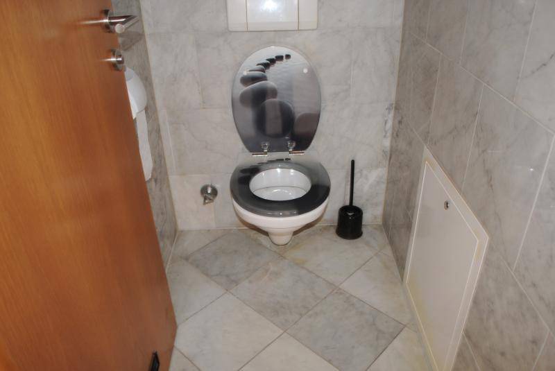 Separates WC mit hellen Fliesen, wandhängender Toilette und dekorativem Toilettendeckel.