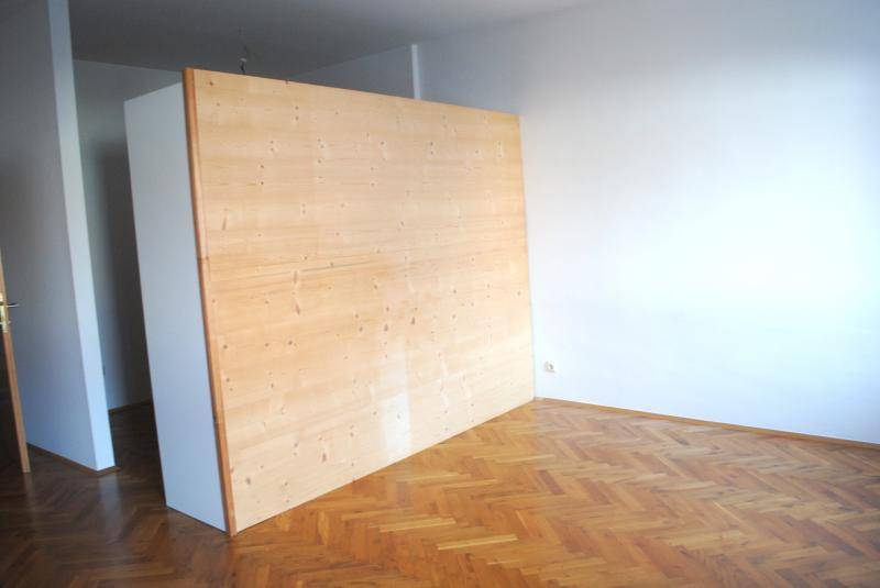 Heller Raum mit Fischgrätparkett und einer großen Holzpaneelwand, die den Raum teilt.