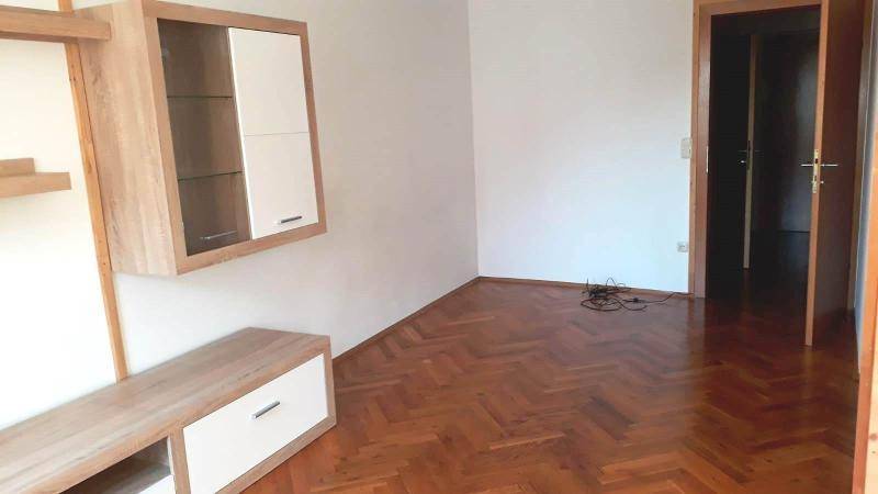 Wohnzimmer mit modernen Holzmöbeln, Fischgrätparkett und offener Tür zu einem weiteren Raum.