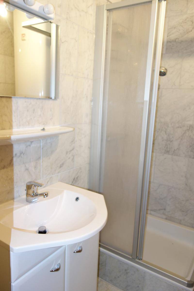 Gefliestes Badezimmer mit Eckwaschbecken, Spiegelschrank und Duschkabine mit Glastür.
