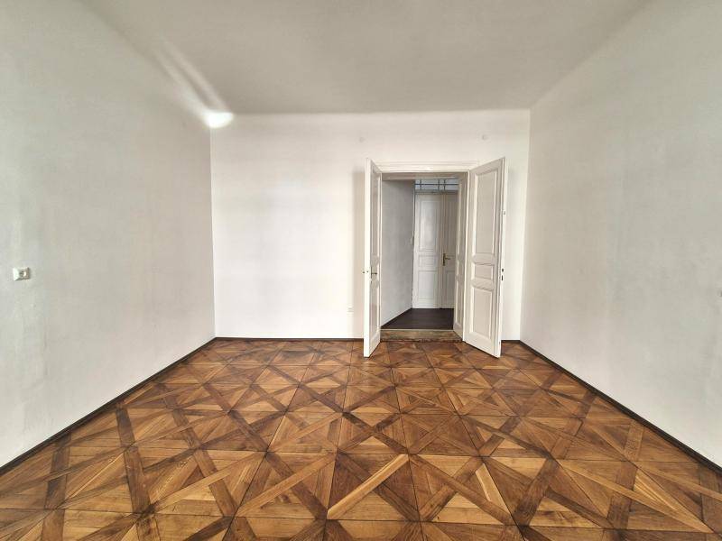 Helles Zimmer mit Parkettboden und einer Doppeltür, die den Übergang zu einem weiteren Raum ermöglicht.