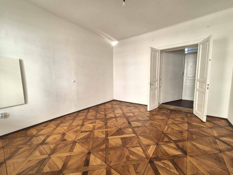 Geräumiges Zimmer mit Parkettboden und einer weit geöffneten Doppeltür, die den Blick in den Flur freigibt.
