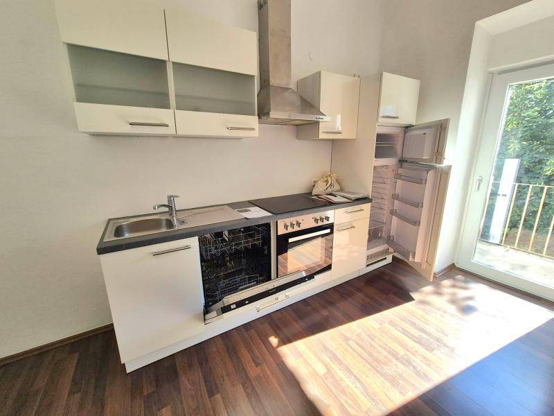 Moderne Einbauküche mit weißen Schränken, integrierten Geräten und Zugang zu einem französischen Balkon.