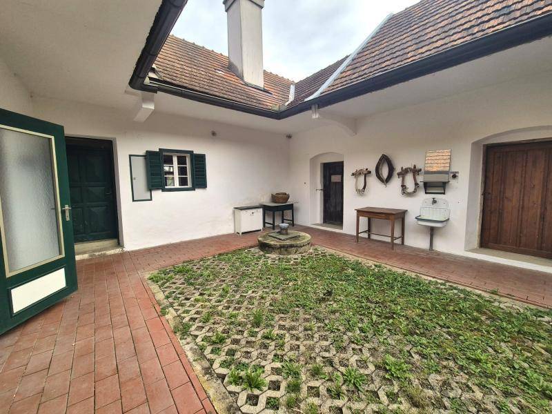 Traditioneller Innenhof mit Ziegelpflaster und begrünten Flächen, umgeben von weißen Wänden.