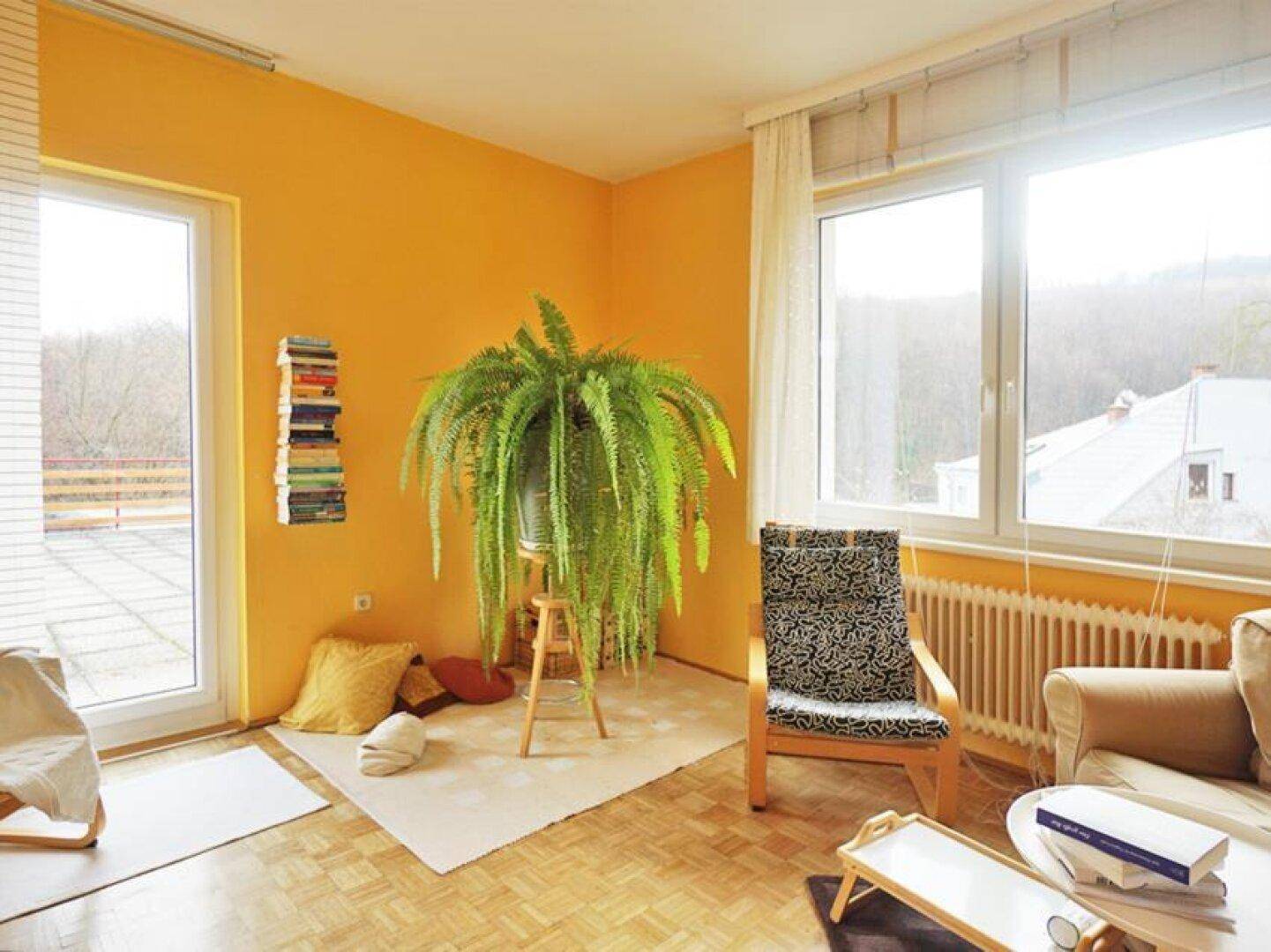 Helles Wohnzimmer mit gelben Wänden, Parkettboden und großem Fenster mit Terrassenzugang.