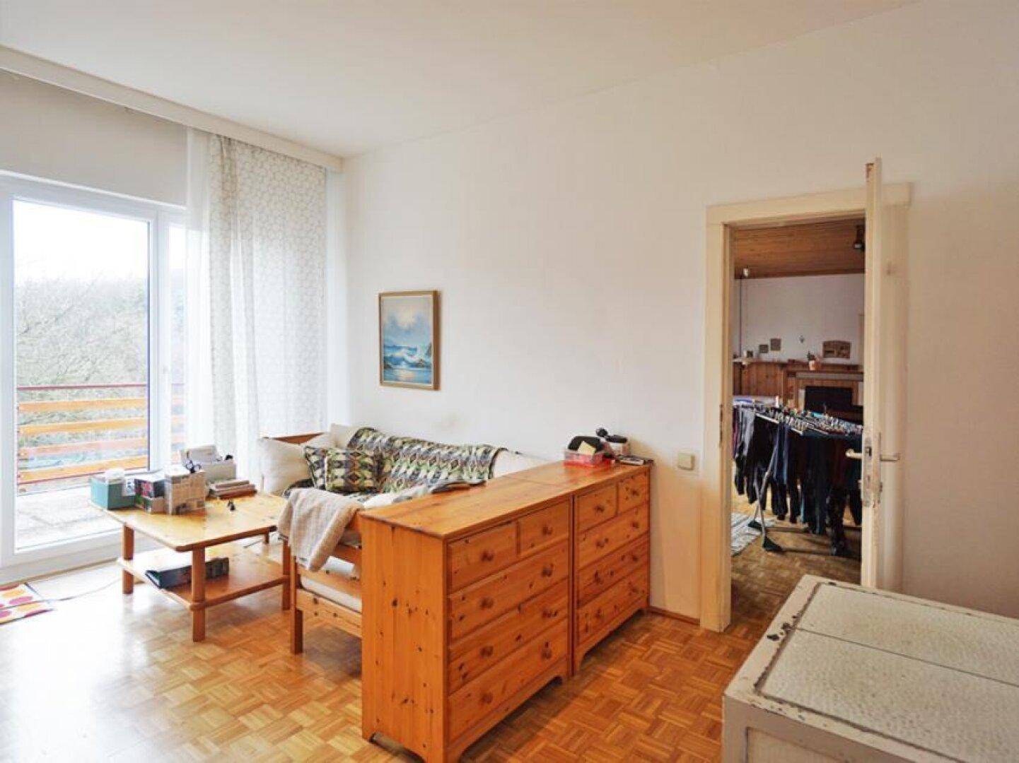 Heller Raum mit Parkettboden, Holzkommode und Zugang zu einem weiteren Zimmer.