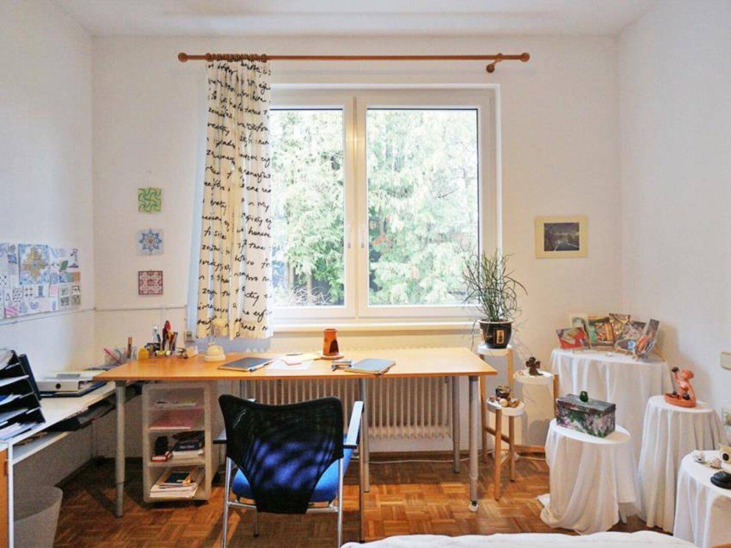 Helles Arbeitszimmer mit Parkettboden, großem Fenster und Blick ins Grüne.