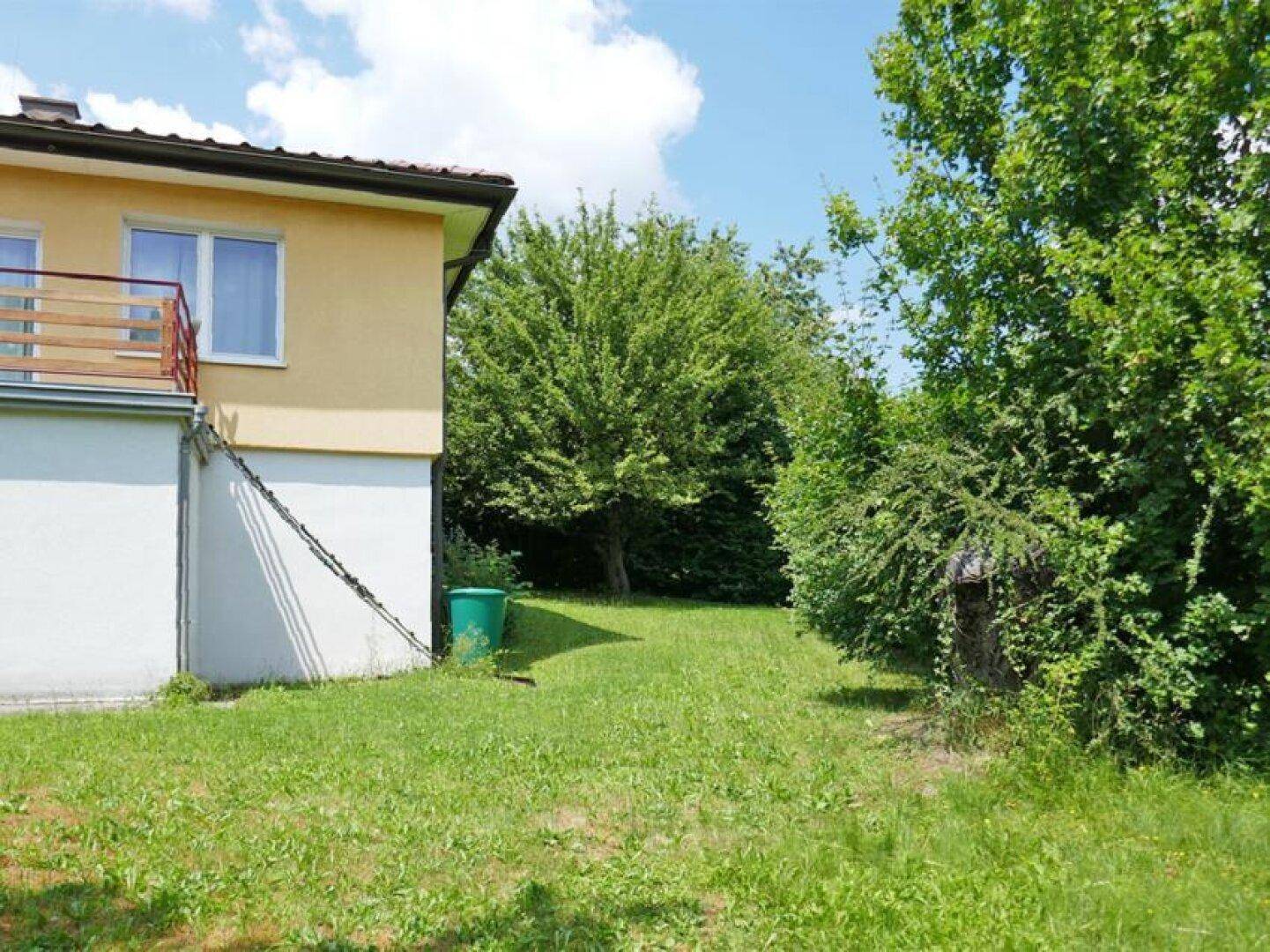 Seitenansicht des Hauses mit gelber Fassade, gepflegtem Rasen und einem kleinen Balkon im Obergeschoss.