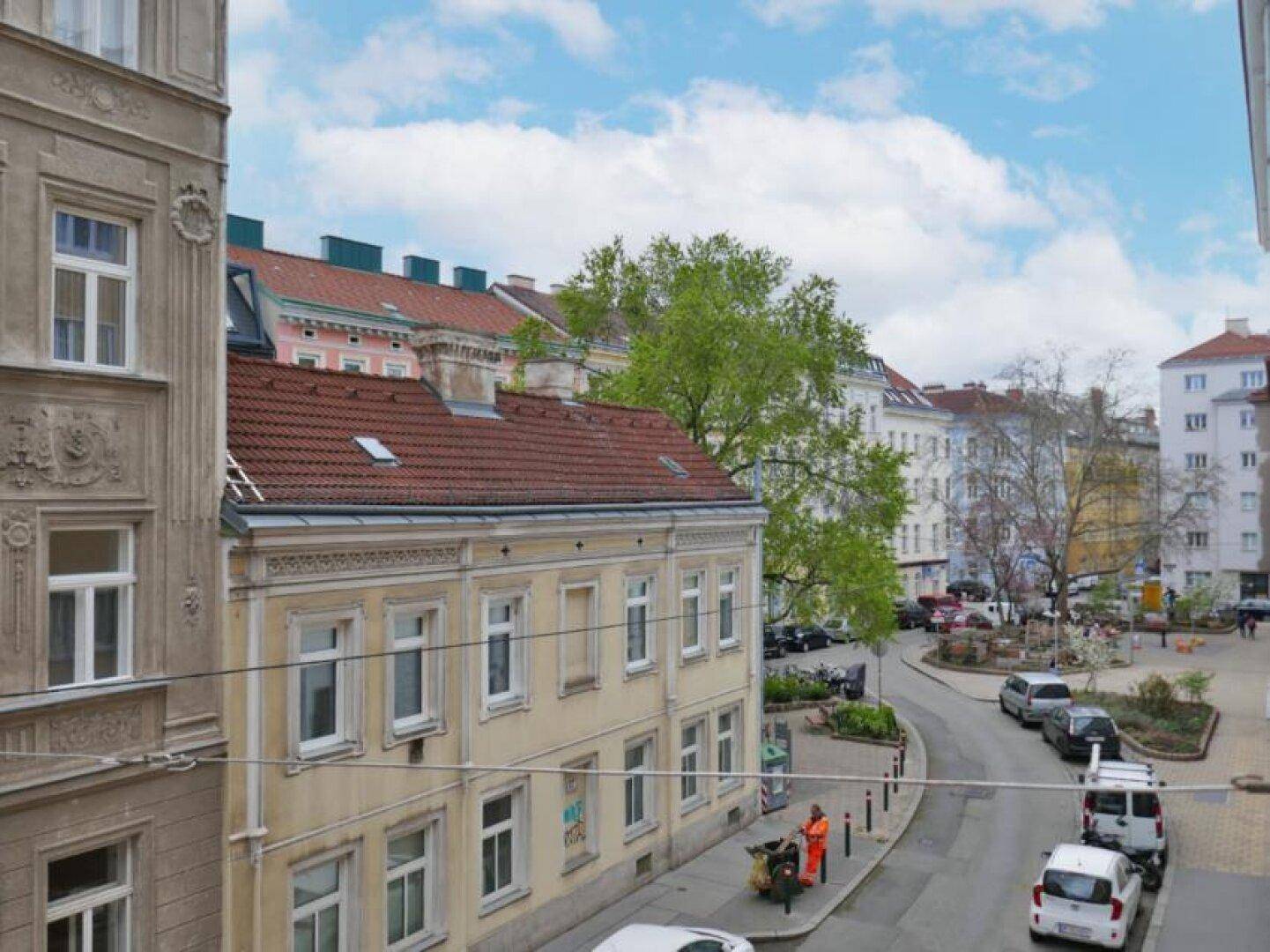 Blick aus dem Fenster auf eine belebte Stadtstraße mit historischen Gebäuden und parkenden Autos.