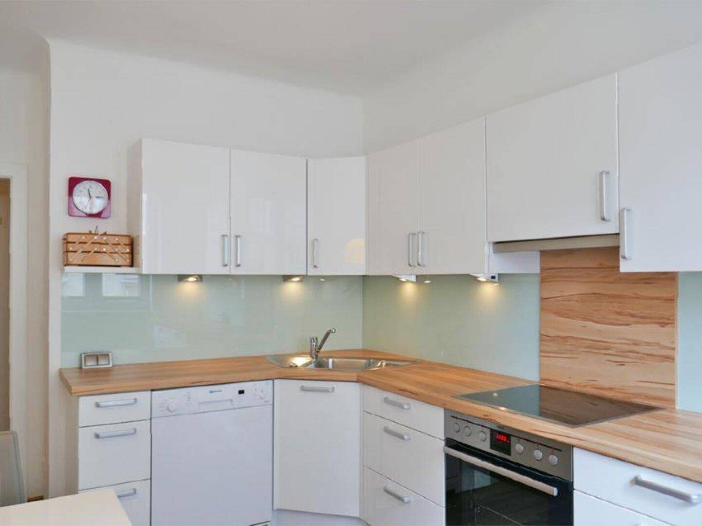 Moderne weiße Einbauküche mit Holz-Arbeitsplatten, integrierten Geräten und indirekter Beleuchtung.