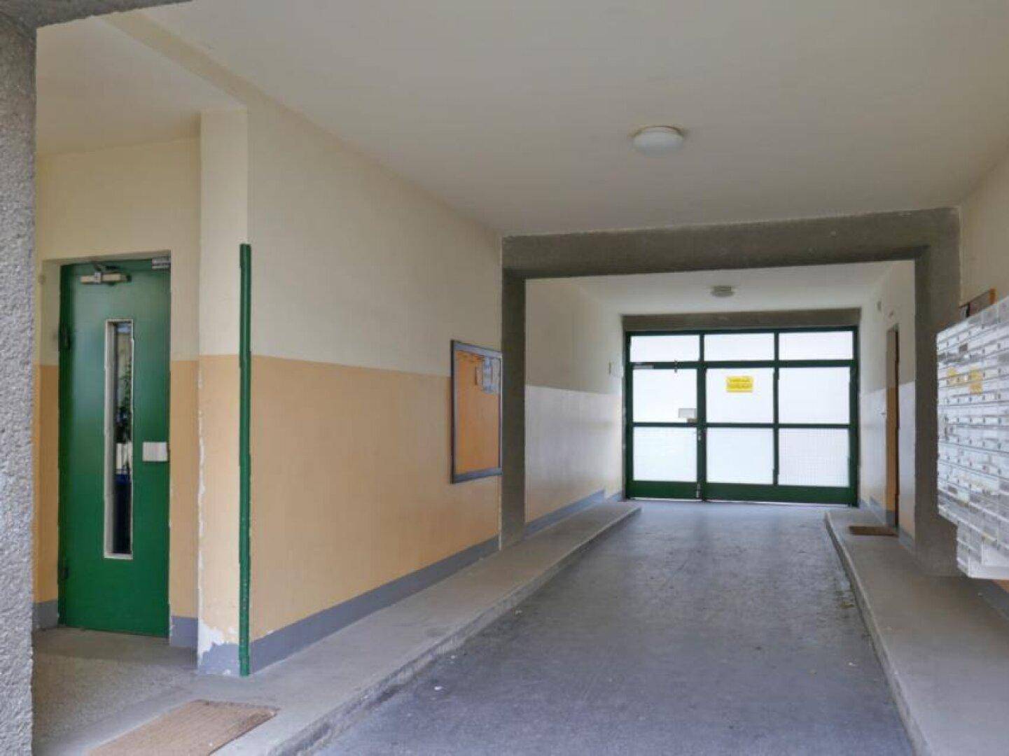 Barrierefreier Eingangsbereich eines Gebäudes mit Rampe und großer Glastür.