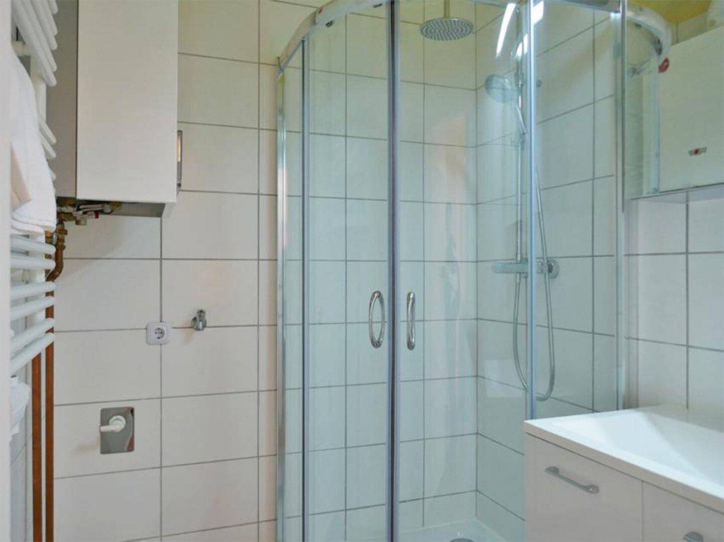 Modernes Badezimmer mit Duschkabine aus Glas, weißen Fliesen und einem beheizten Handtuchhalter.