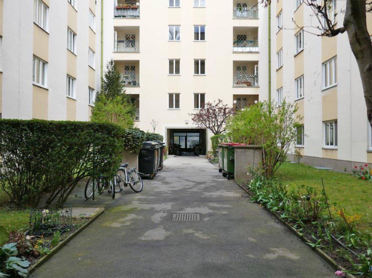 Gepflegter Innenhof eines Wohngebäudes mit Grünflächen, Sträuchern und einem befestigten Weg.