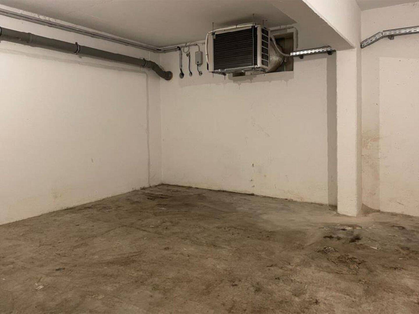 Unfertiger Kellerraum mit Betonboden und sichtbaren Installationen an der Decke und Wänden.