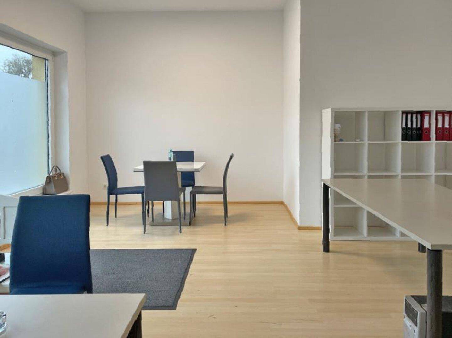 Geräumiger Bürobereich mit hellem Holzboden, einem Esstisch und einem weißen Regal an der Wand.