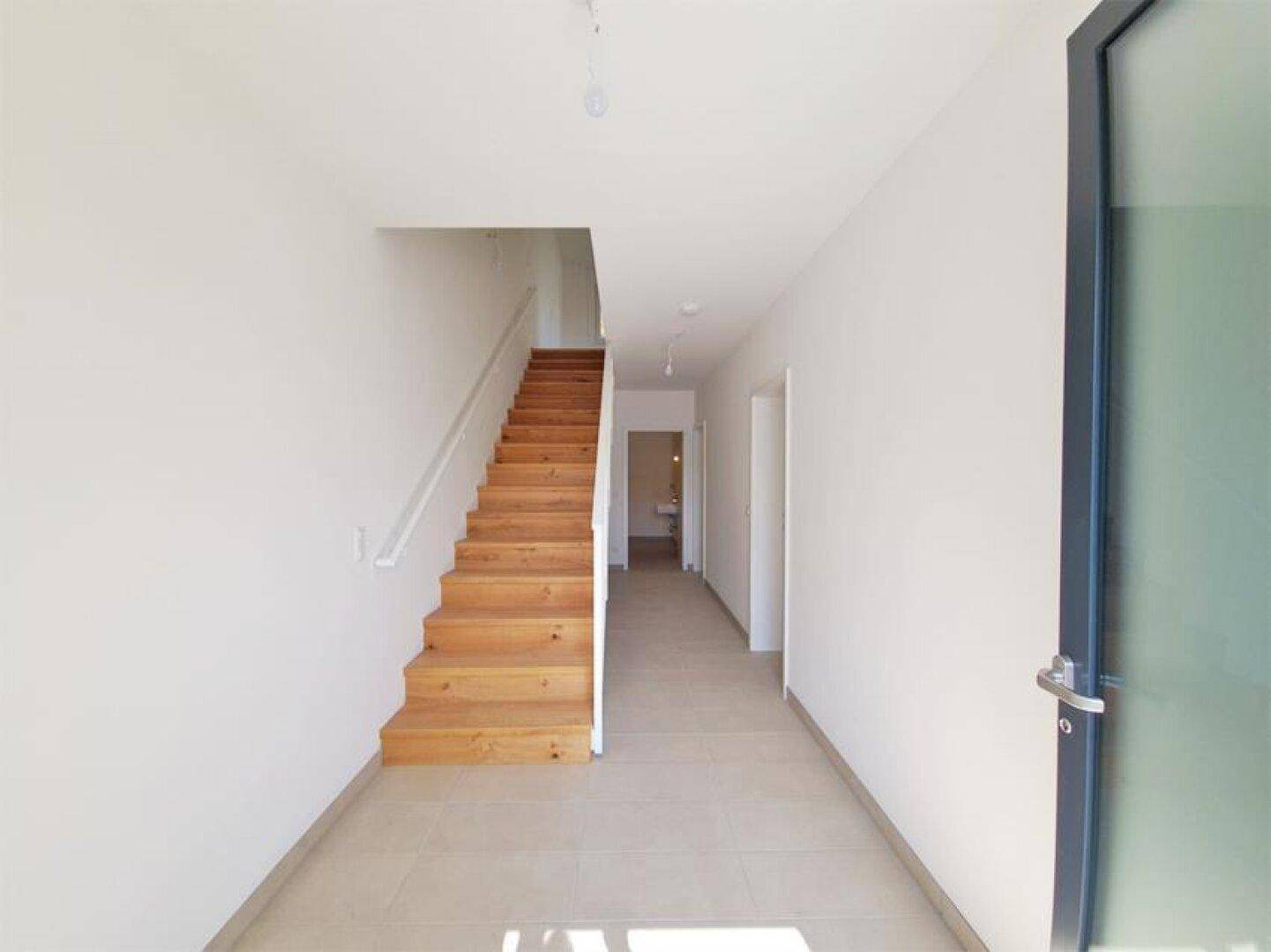 Geräumiger Eingangsbereich mit Holztreppe und Fliesenboden, der zu den oberen Etagen führt.