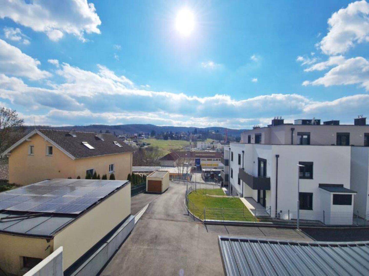 Panoramablick über eine Wohnsiedlung mit grünen Hügeln im Hintergrund unter blauem Himmel.