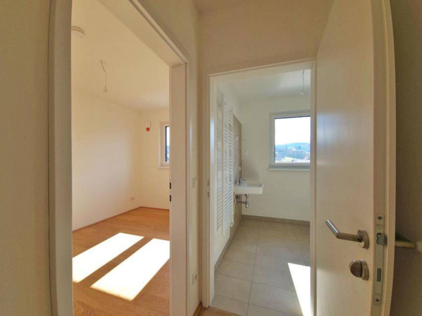 Heller Flur mit Holzboden, der zu einem Schlafzimmer und einem Badezimmer führt.