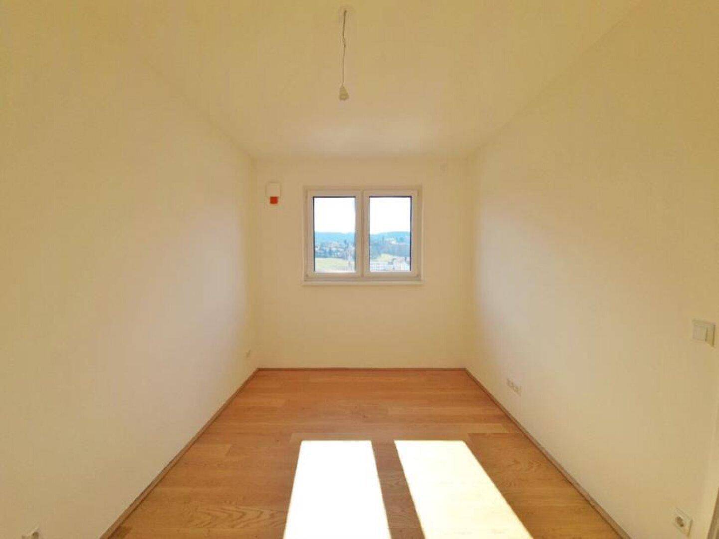 Sonniges, leeres Zimmer mit Holzboden und einem Fenster, ideal als Schlaf- oder Kinderzimmer.