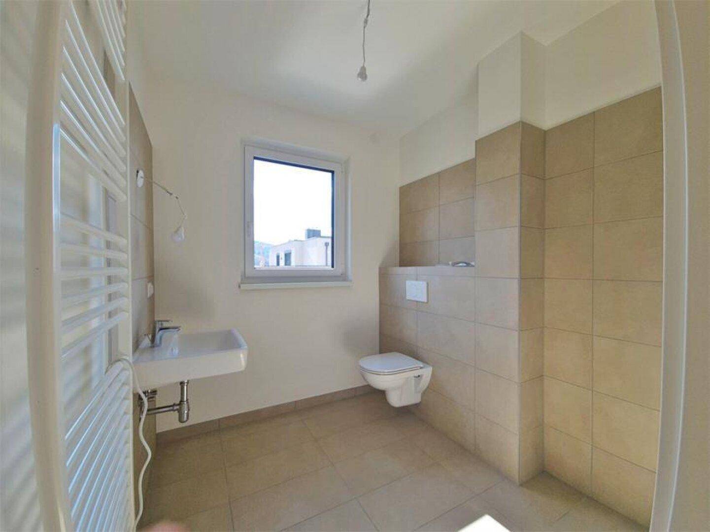 Modernes Badezimmer mit Wand-WC, Waschbecken, Handtuchheizkörper und beigefarbenen Fliesen.