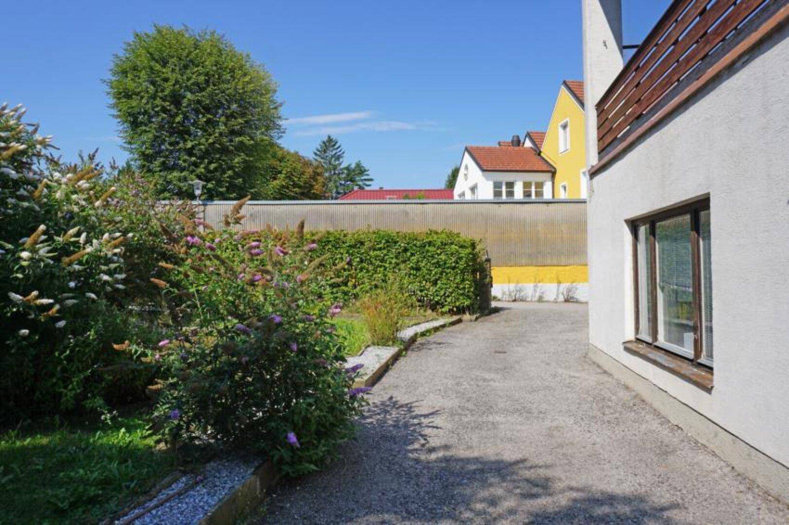 Gartenweg aus Kies neben üppigen Sträuchern und Hecken, mit Blick auf Nachbargebäude.
