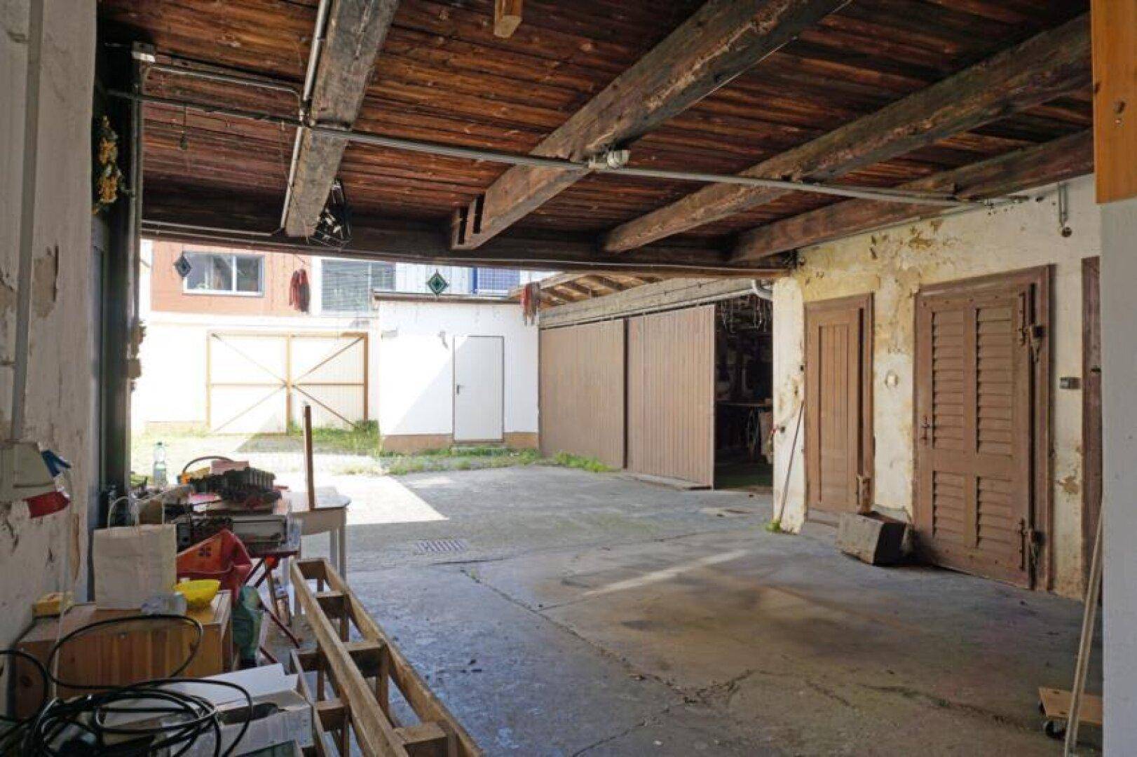 Geräumige Garage oder Werkstatt mit Holzbalkendecke und Betonboden, renovierungsbedürftig.