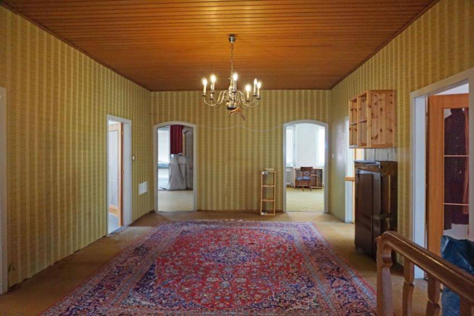 Geräumiger Wohnbereich mit gemusterter Tapete, Holzbalkendecke und traditionellem Teppich.