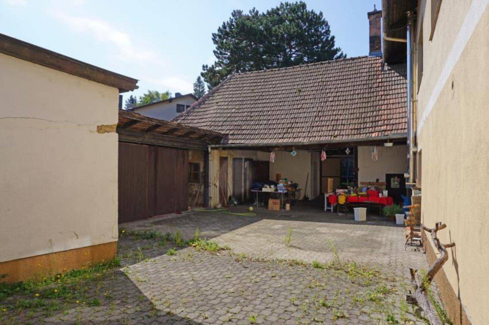 Gepflasterter Innenhof zwischen Gebäuden mit verschiedenen Türen und einem überdachten Bereich.