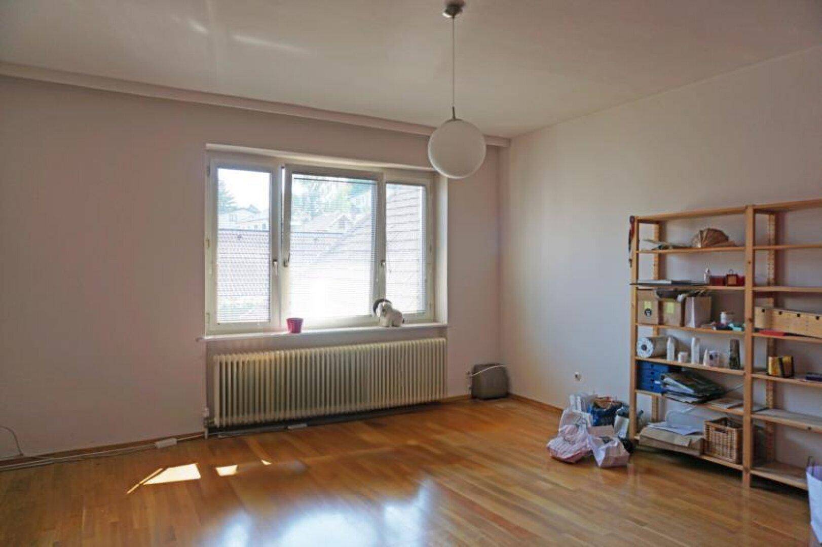 Helles Schlafzimmer mit Parkettboden und großem Fenster, bereit für individuelle Gestaltung.