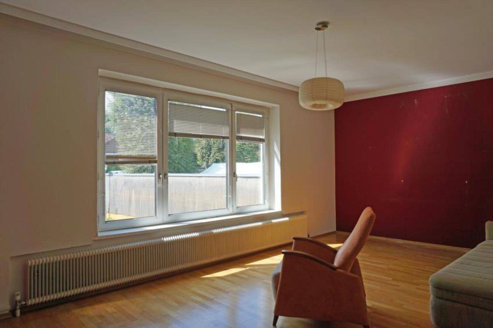 Helles Zimmer mit Holzboden und einer roten Akzentwand, die einen Farbtupfer setzt.