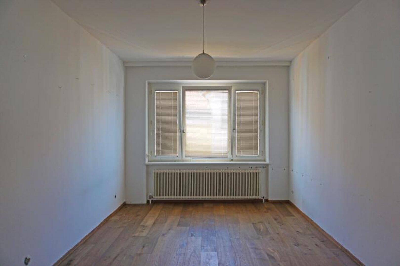 Helles Zimmer mit Parkettboden und Fenster, das eine angenehme Atmosphäre schafft.