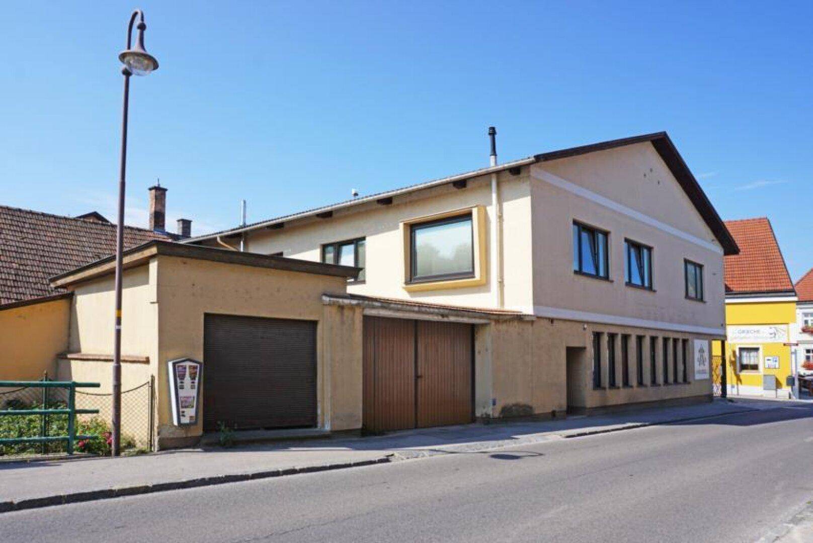 Rückansicht des Gebäudes mit Garagen und weiteren Fenstern, unter blauem Himmel.