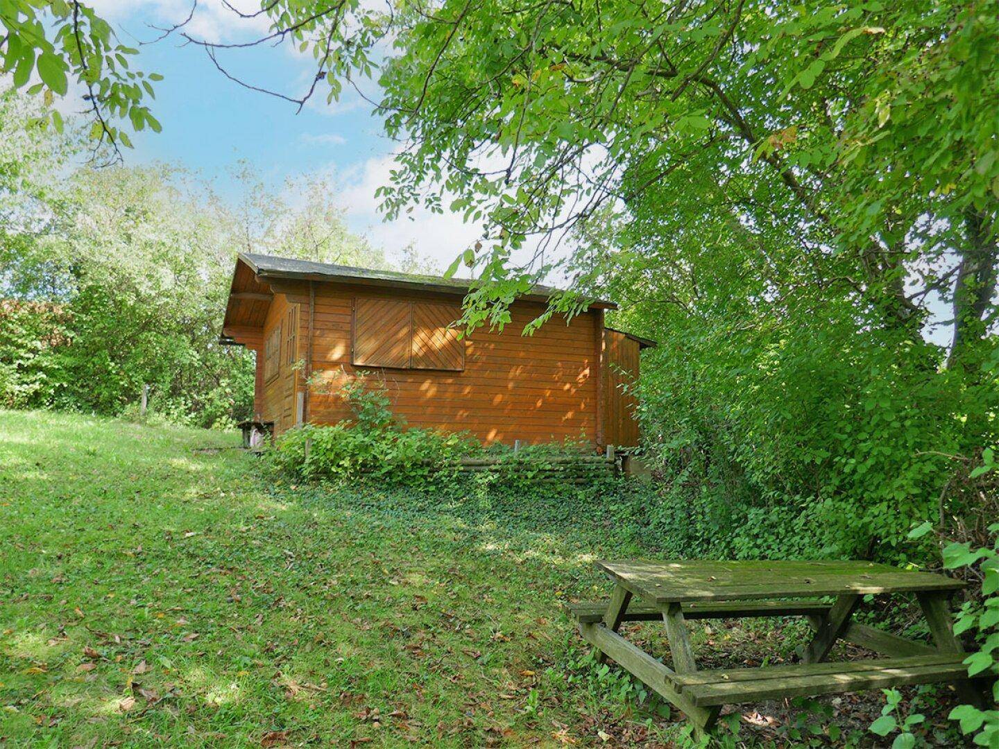 Rustikaler Holzschuppen im Garten mit einem Picknicktisch, ideal für gemütliche Stunden im Freien.