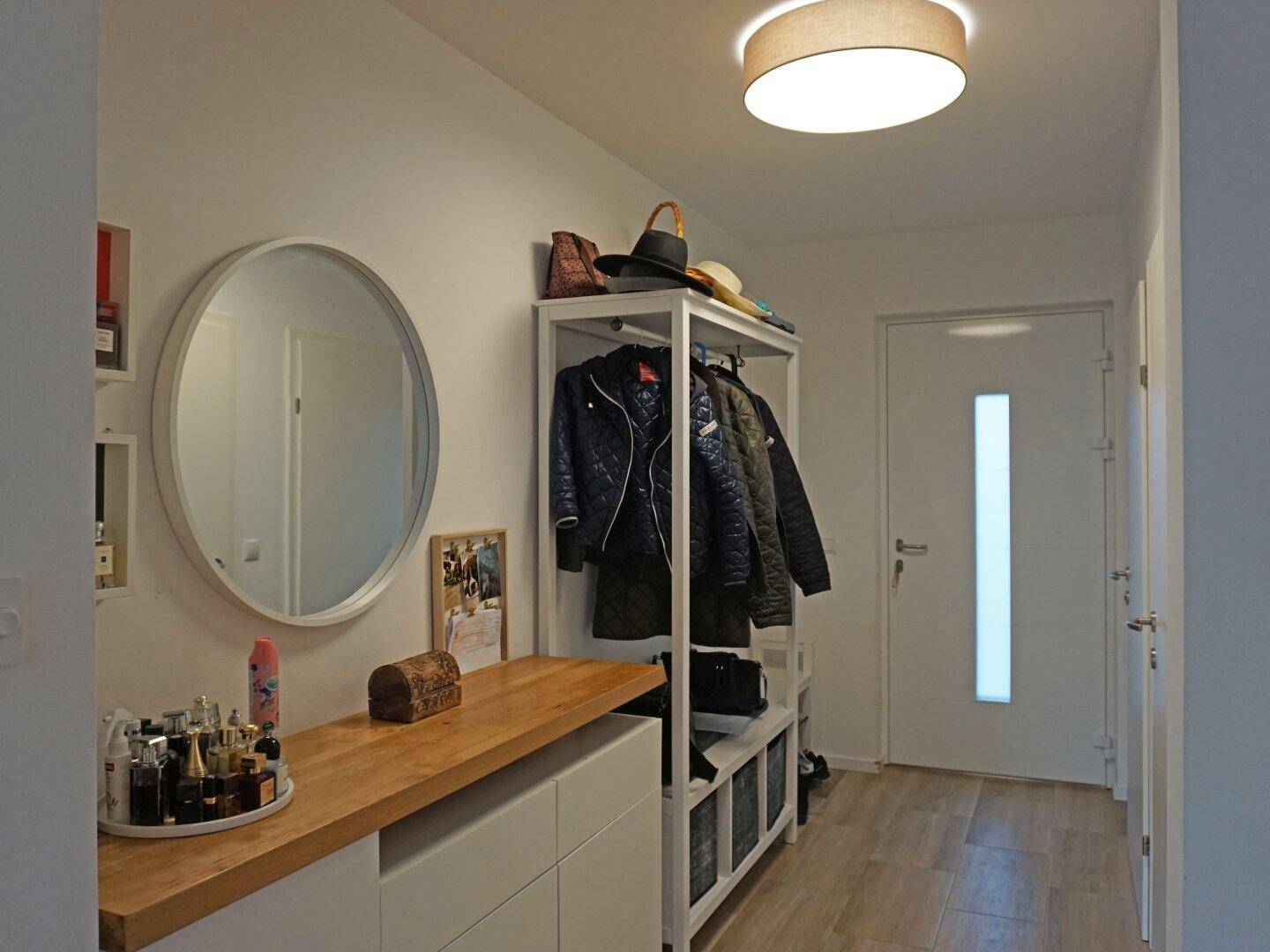 Heller Eingangsbereich mit Garderobe, Spiegel und Holzablage, der zu den weiteren Räumen führt.