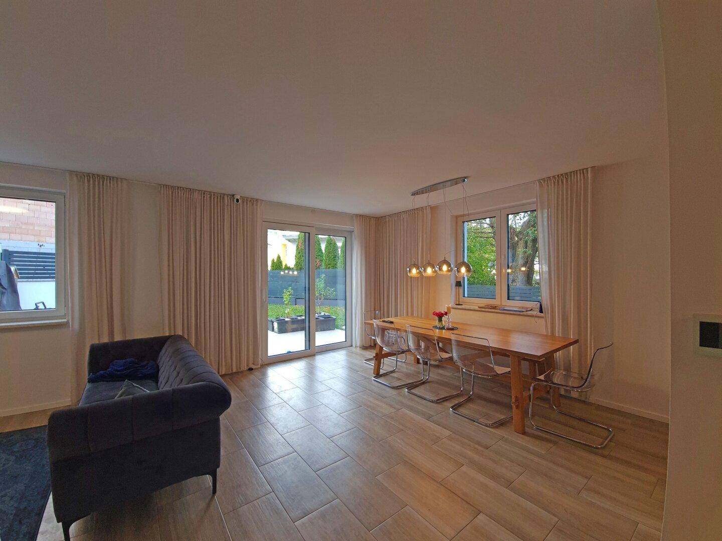 Geräumiger Wohn-Essbereich mit Zugang zum Garten und großen Fenstern, ausgestattet mit modernen Fliesen.