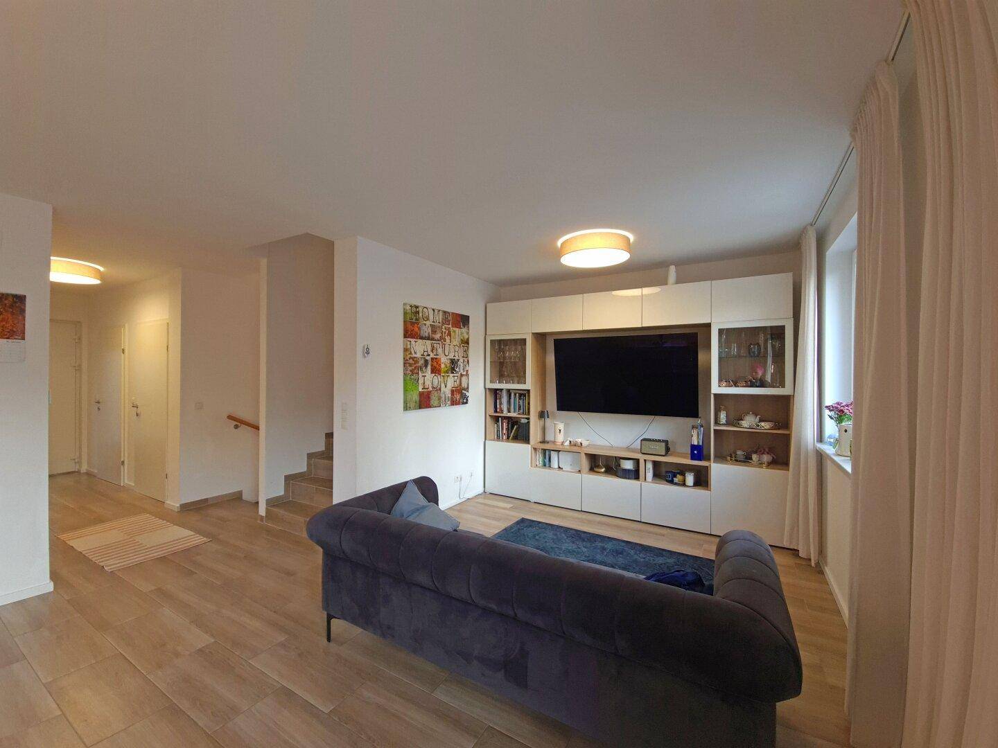 Gemütliches Wohnzimmer mit großem Sofa, TV-Möbel und hellem Bodenbelag.