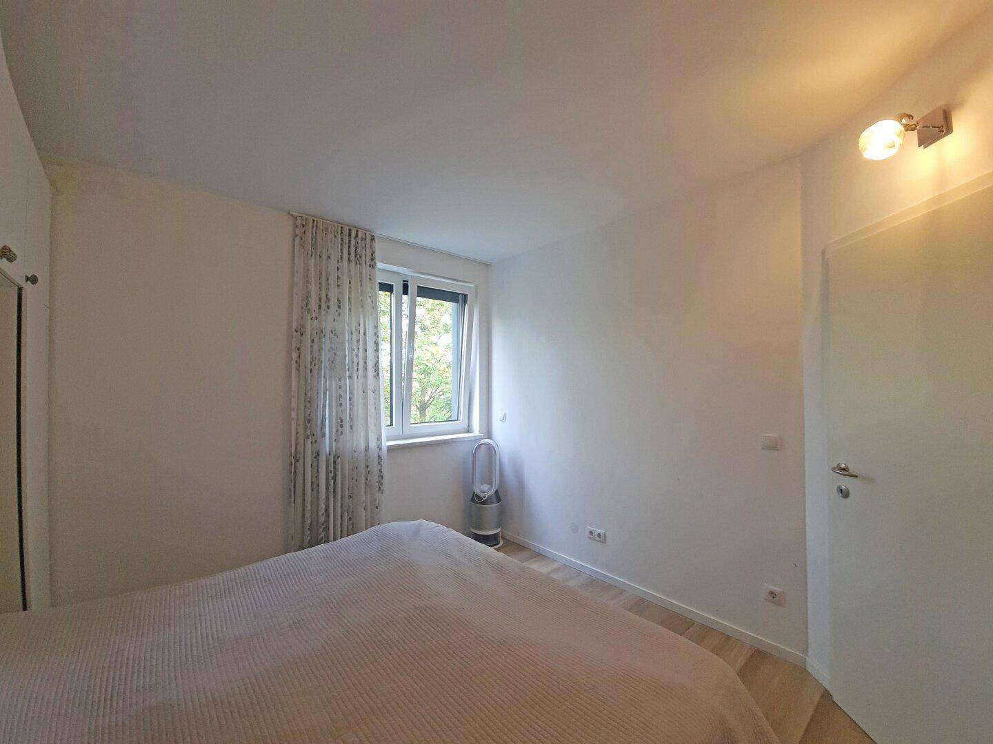 Schlafzimmer mit Doppelbett und Fenster, das viel Tageslicht hereinlässt.