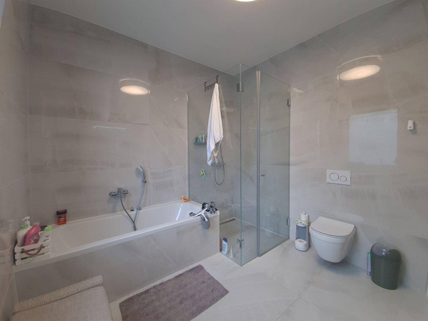 Geräumiges Badezimmer mit Badewanne, Duschkabine und wandhängendem WC.