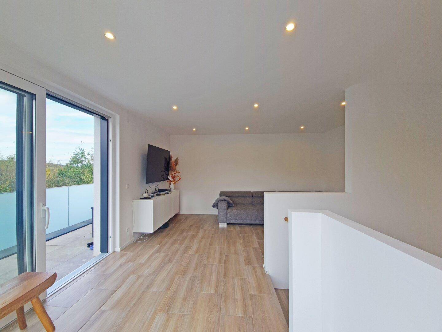 Wohnzimmer mit großem Fernseher und Schiebetür zum Balkon oder zur Terrasse.
